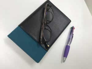 机の上にあるノート、めがね、ペン